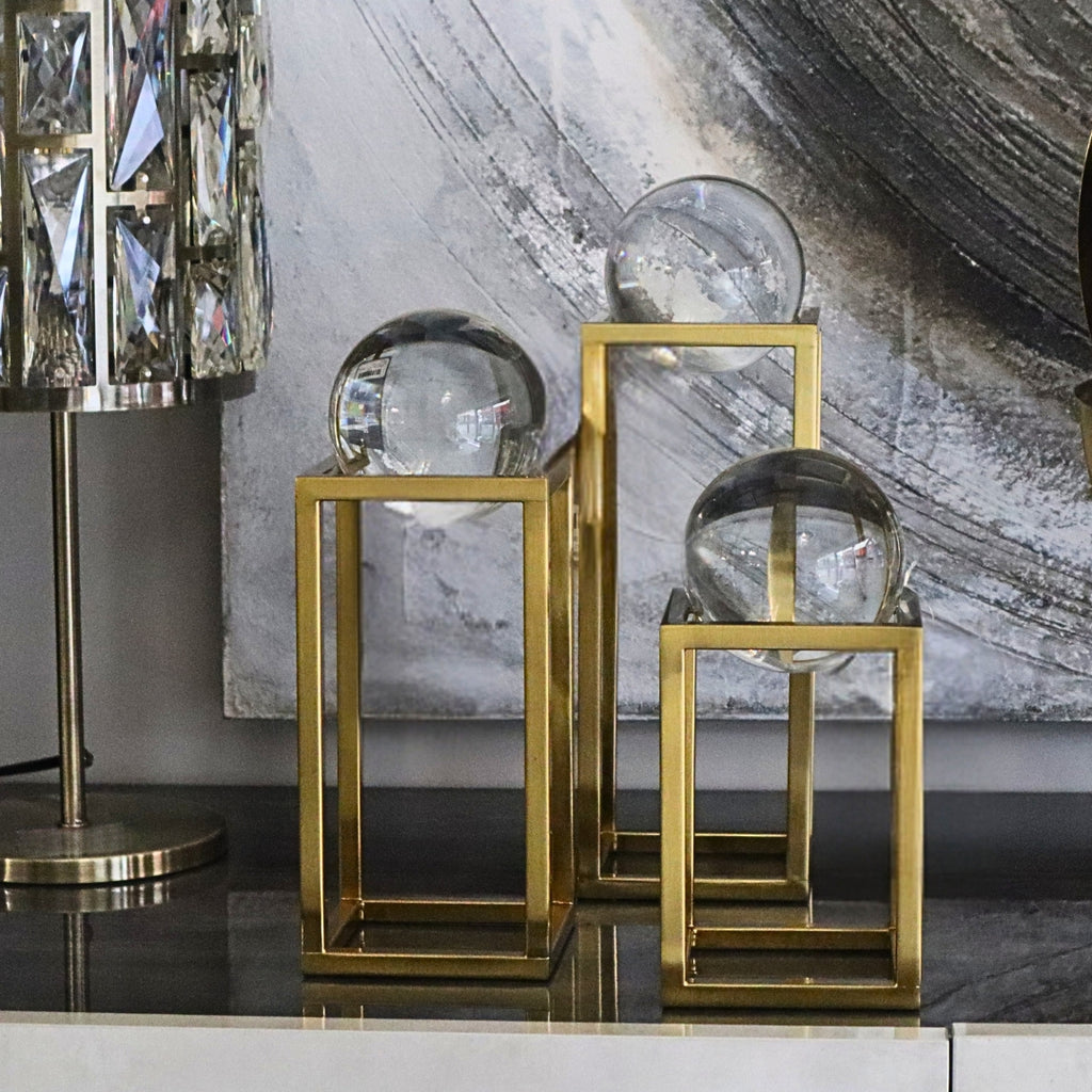 Decorative glass spheres on gold stands against a marble wall.