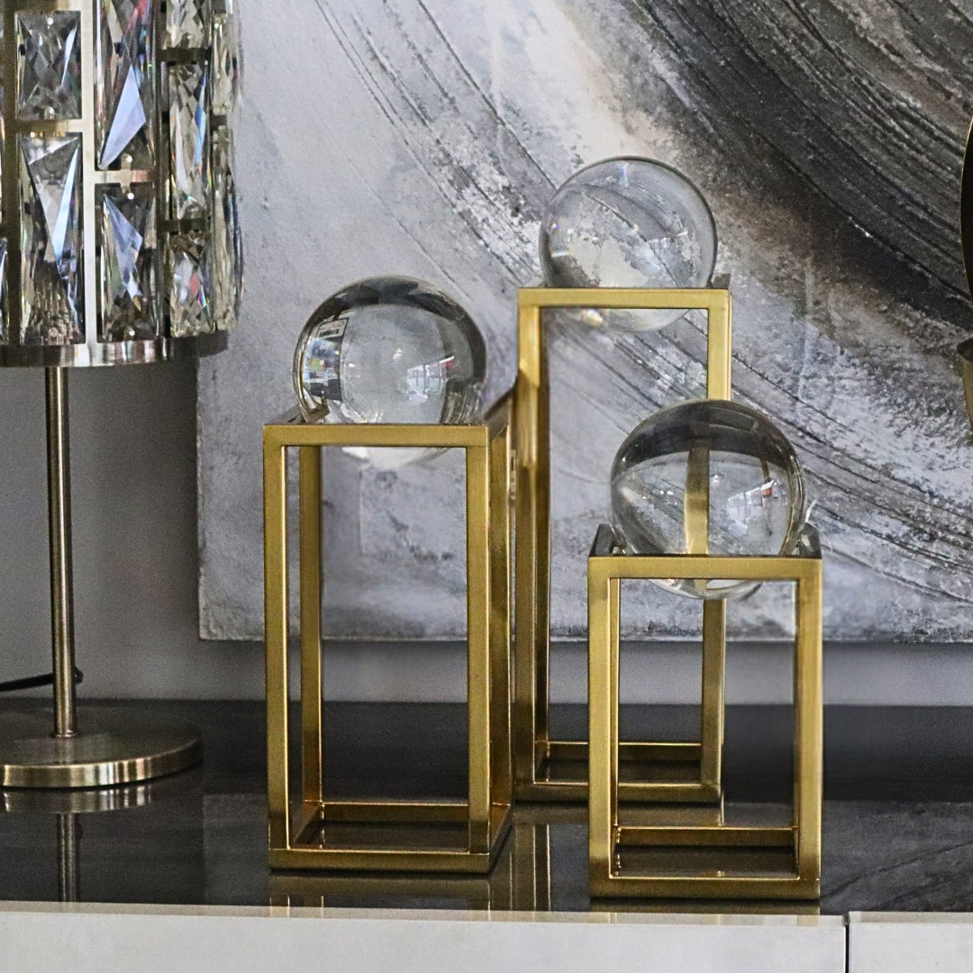 Decorative glass spheres on gold stands against a marble wall.