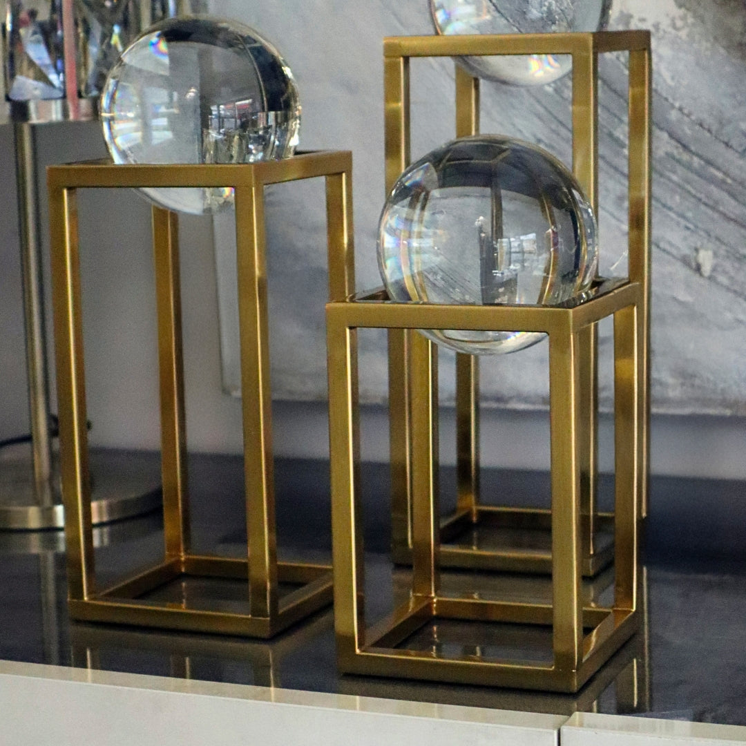 Two gold metal stands with crystal balls on a reflective surface.