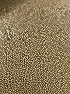 A close-up of a textured material featuring a repeating pebble or reptile-scale pattern in black on a warm tan or beige background.