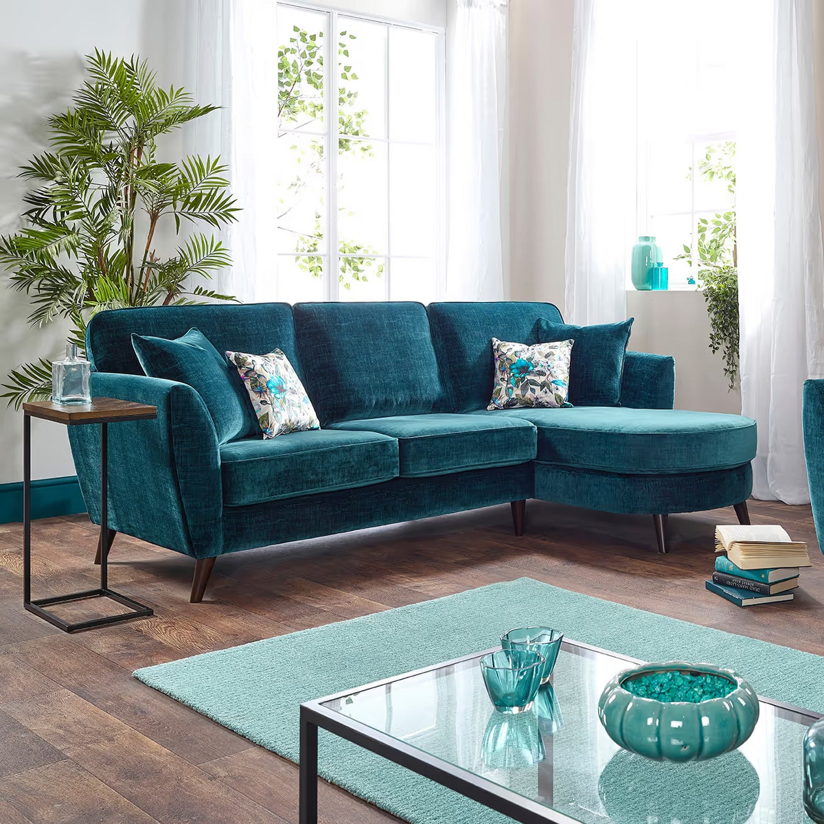 Modern living room with teal sectional sofa and armchair, glass coffee table, and decorative items.