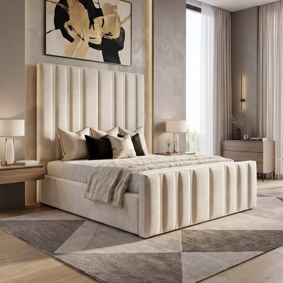 A modern bedroom featuring a cream upholstered bed with vertical channel tufting, set against a textured gray wall with abstract black and gold wall art. The room includes light wood flooring, matching geometric area rugs, bedside tables with lit lamps, and a large window with sheer curtains.