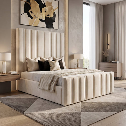 A modern bedroom featuring a cream upholstered bed with vertical channel tufting, set against a textured gray wall with abstract black and gold wall art. The room includes light wood flooring, matching geometric area rugs, bedside tables with lit lamps, and a large window with sheer curtains.